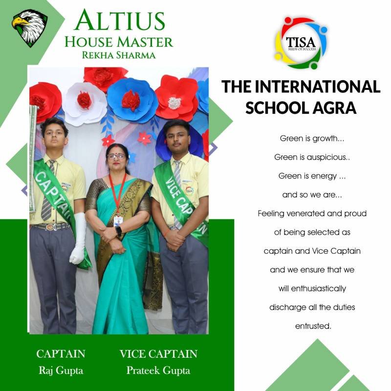 Photo of raj gupta (captain) and prateek gupta (vice captain) of altius house at the international school agra, standing on either side of house master rekha sharma. They are posed in front of a colorful backdrop decorated with large red, white, and blue paper flowers. The students wear yellow shirts, grey trousers, and green sashes labeled "captain" and "vice captain". Rekha sharma is dressed in a green and blue saree that complements the house color. Text on the right speaks about the symbolism of green and expresses pride in being selected as leaders, with a commitment to fulfilling their duties. The tisa logo is displayed at the top.