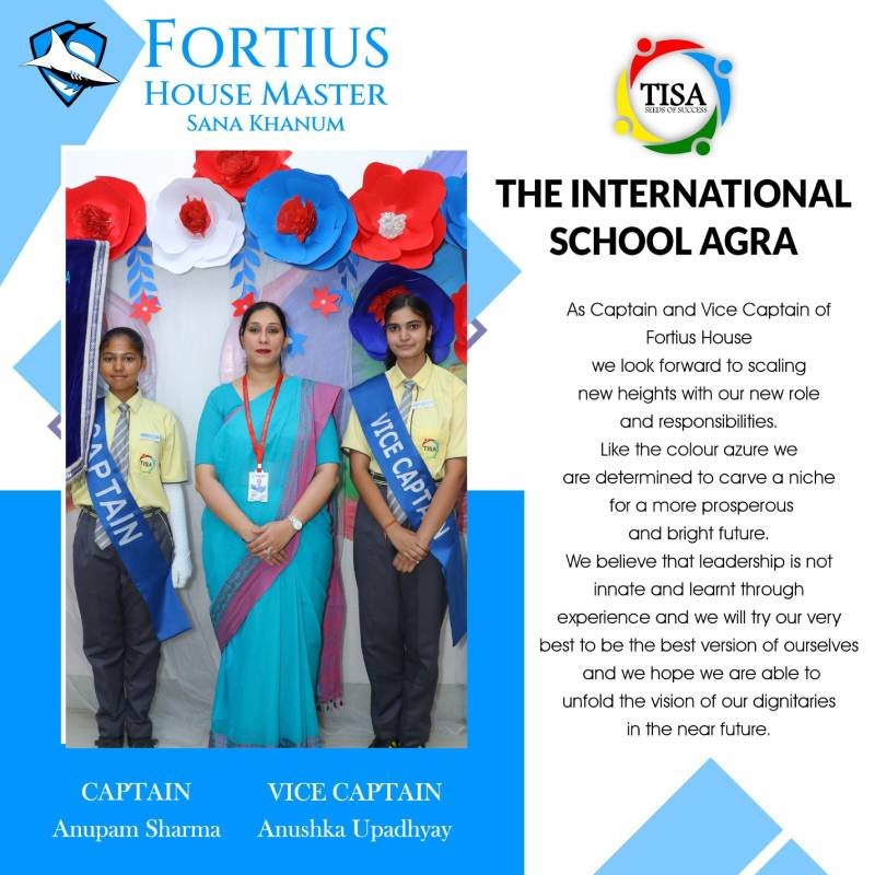 Photograph of anupam sharma (captain) and anushka upadhyay (vice captain) of fortius house at the international school agra, standing with house master sana khanum. They are positioned in front of a decorative backdrop featuring large red, white, and blue paper flowers. The students wear yellow shirts, grey trousers, and blue sashes labeled "captain" and "vice captain". Sana khanum is dressed in a blue saree with a pink border. The right side features the tisa logo and a message about embracing leadership, aiming for excellence, and looking forward to a bright future. The theme highlights the color azure as a symbol of prosperity and determination.