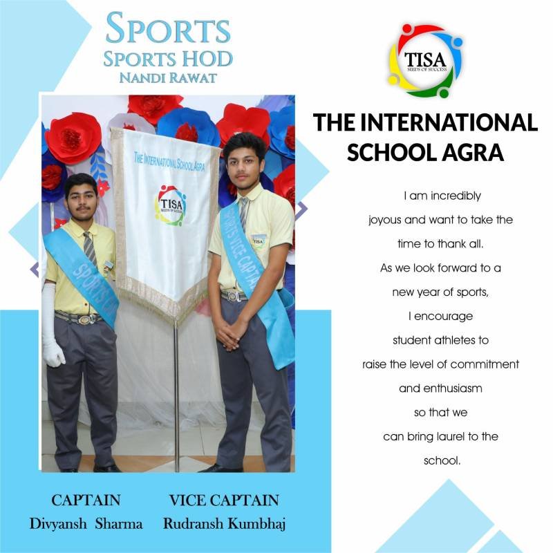 Group photo of divyansh sharma (captain) and rudransh kumbhaj (vice captain), student leaders of the sports council at the international school agra. Both students are wearing yellow shirts, grey trousers, and light blue sashes labeled "sports captain" and "athletic captain" respectively. They stand on either side of a banner with the school logo. The background is decorated with red, white, and blue paper flowers. A message on the right expresses excitement for the upcoming sports year, encouraging student athletes to show commitment and enthusiasm to bring pride to the school. The school logo and name are prominently displayed.