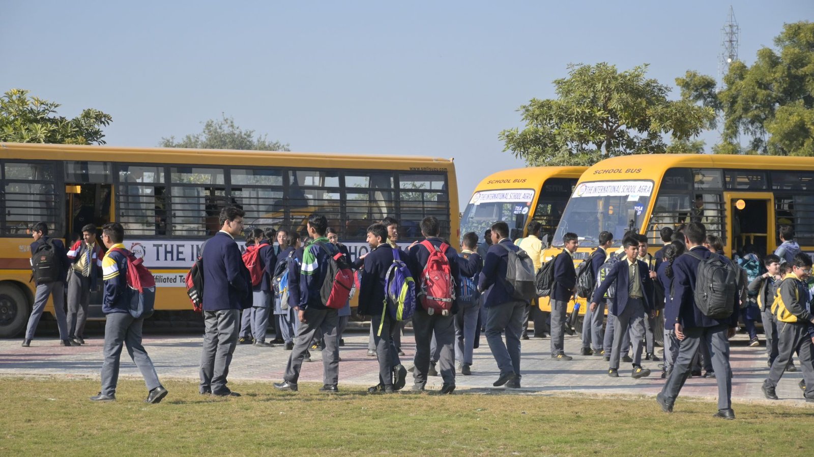 About 10 Students at tisa, the best school in agra, gather around yellow school buses during morning arrival.