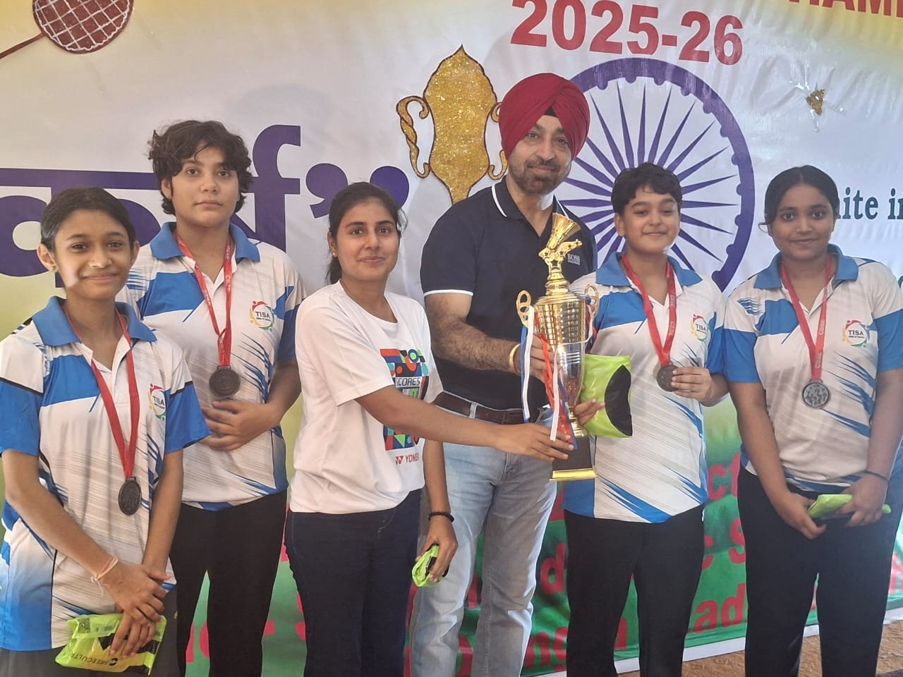 The International School Agra’s Under-19 Girls Badminton Team receiving the bronze trophy from their coach after winning at the CBSE National Badminton Championship 2025 in Gohana, Haryana.